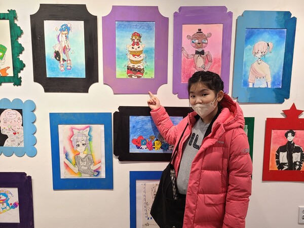 미술전시회에 참가한 온누리M센터 지역아동센터 학생이 자신이 그린 그림을 가리키며 사진 촬영을 진행하고 있다(사진 = 김종현 기자)